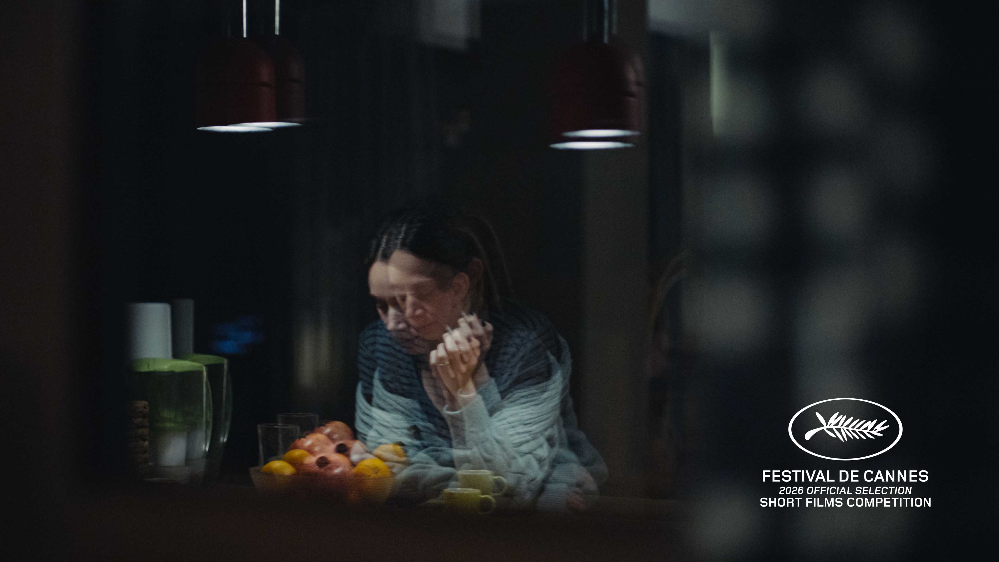 Blurred double exposure of a woman sitting at a table with fruit and cups under dim lights.