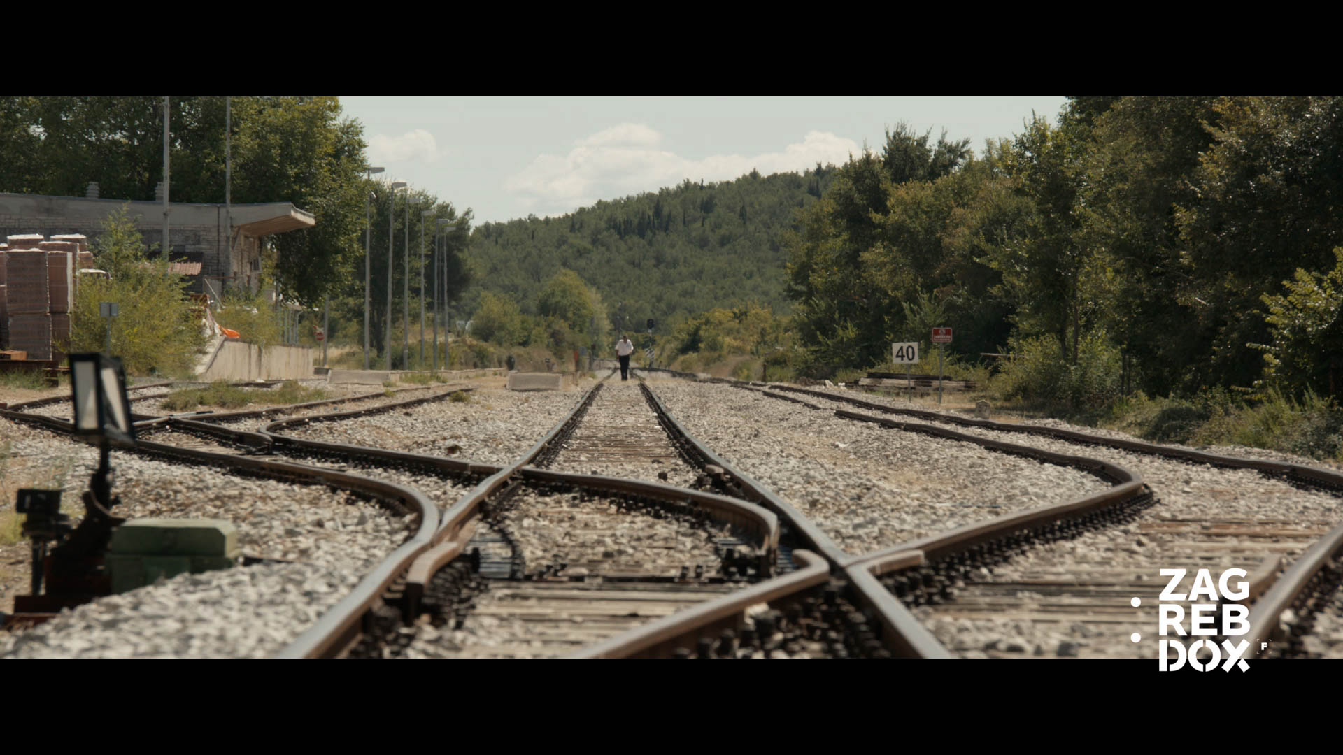 Railroad tracks converging into the distance with a person walking along the center track.