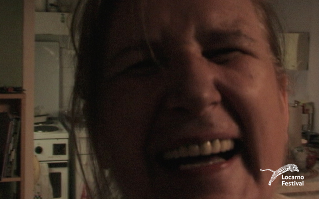 Close-up of a person laughing with eyes closed in a dimly lit room.